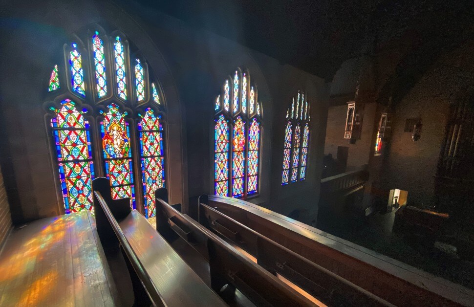 What are church bylaws? Sun rays beam into nine beautiful panels of glass stained red, yellow, green and pink inside a church with wooden pews