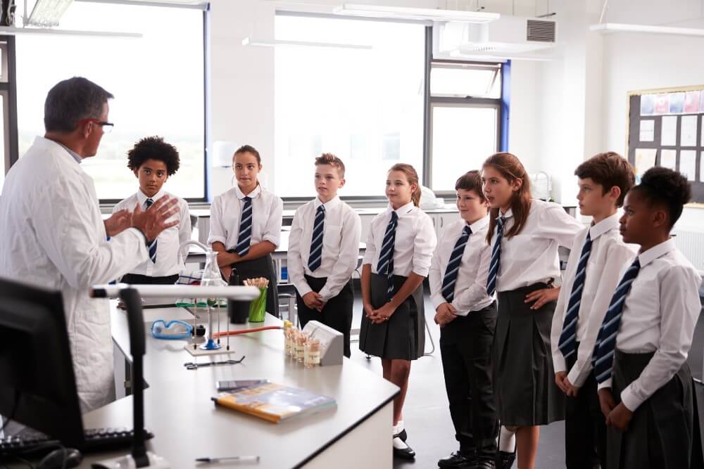 A science teacher addresses eight middle-school students dressed in private school uniforms with white dress shirts and ties