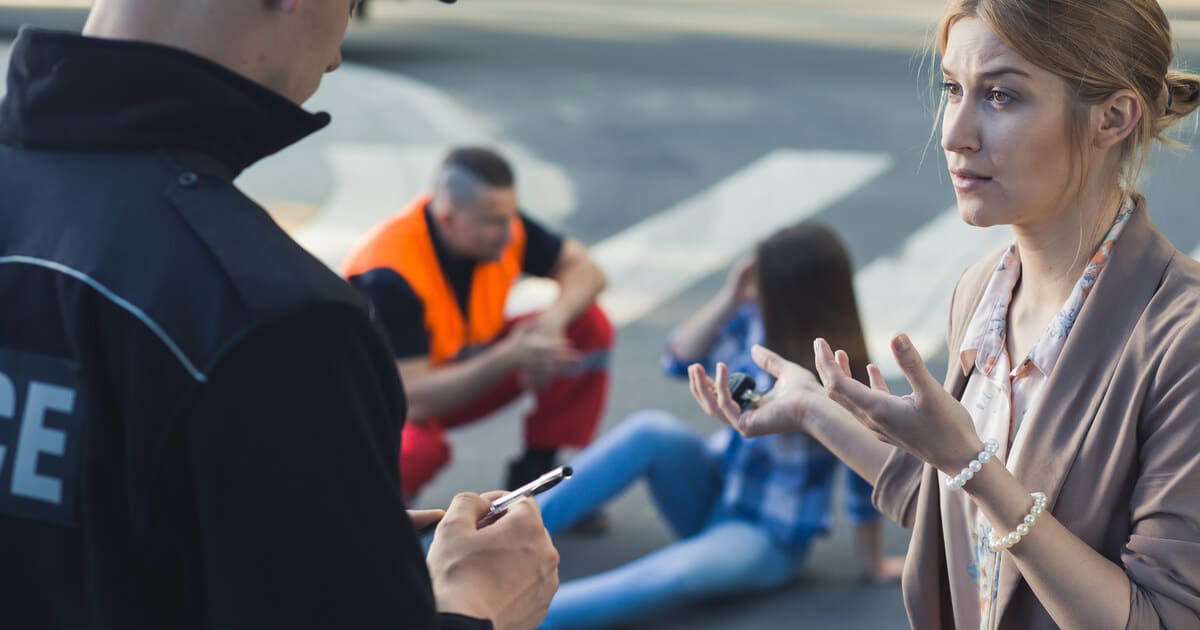 A woman is talking to a police officer at the scene of an accident because she knows what to do if you witness a car accident.