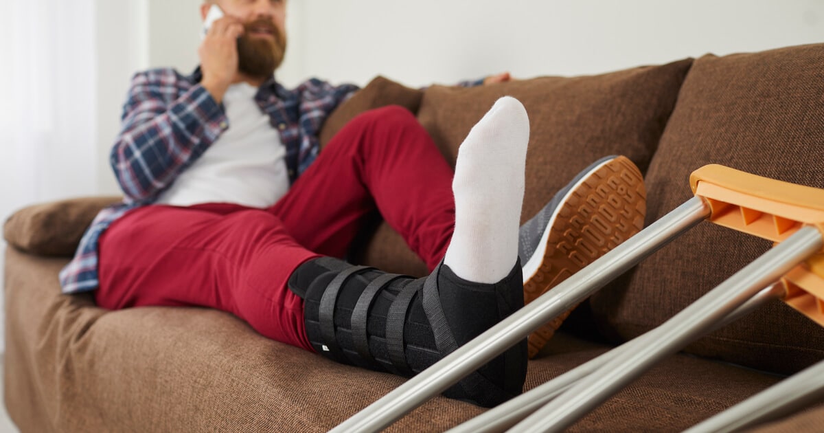 A strong man is sitting on the couch with a workplace injury and is wondering when to hire a workers' comp lawyer.