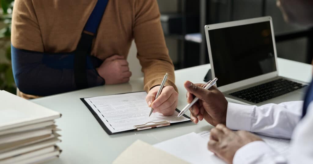 An injured man meets with a workers comp lawyer to secure the claim he deserves after asking, "Will workers comp offer a settlement without a lawyer?"