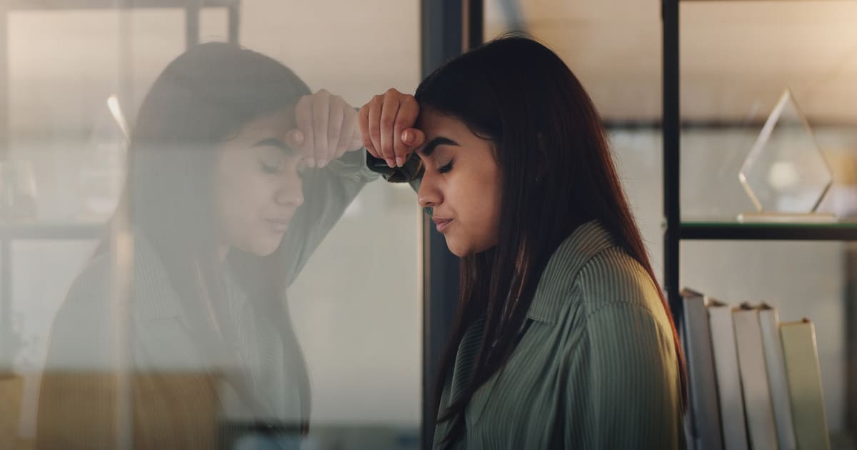 A struggling woman leans her head against the wall and wonders "can you get workers comp for mental health?"