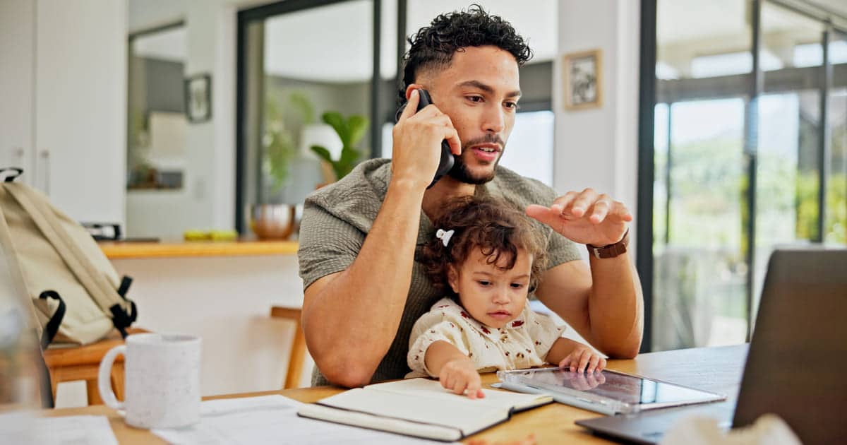 A man who works from home has his daughter sitting on his lap and is reading a blog about workers comp for remote employees.