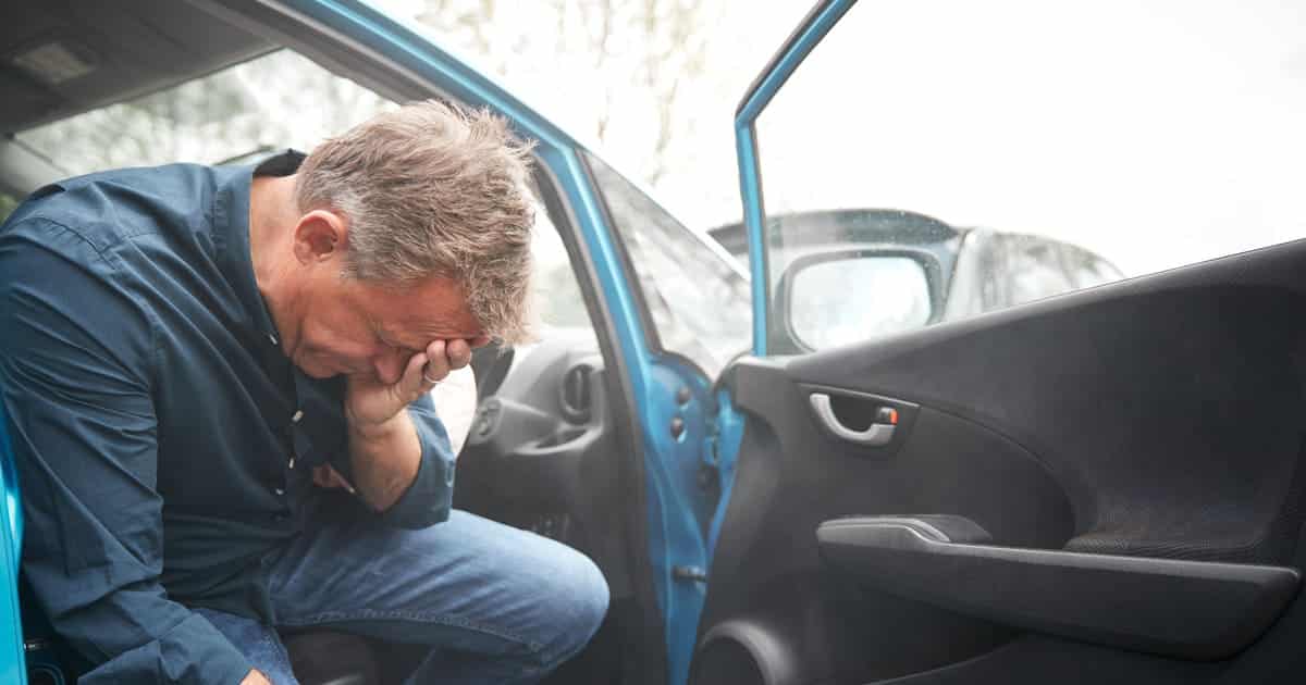 A man holds his head in his hands, distraught in this scenario: car accident, at fault, no insurance.